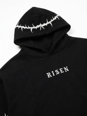 A close-up of a black hoodie featuring a white thorny crown graphic on the hood and the word 'RISEN' in white gothic lettering on the chest, set against a plain white background.